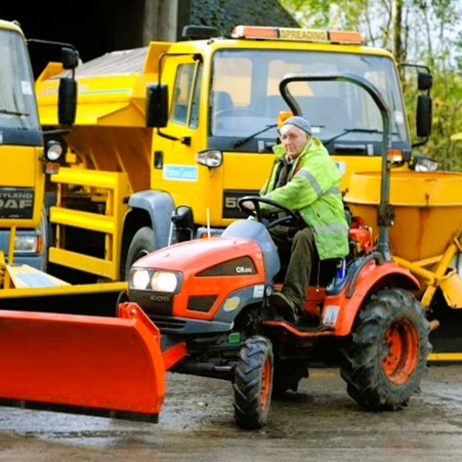 person on tractor in front of gritting lorries