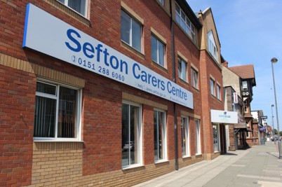 The Sefton Carers Centre building, with a focus on the sign. The building is pictured left of centre, facing towards the right.