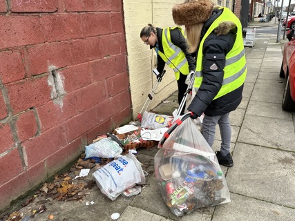 People picking up litter from the streets, including plastic bags and takeaway boxes.