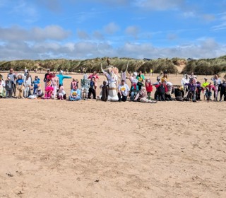 A photo on a beach of statues made of recycled wood and fabric alongside people. 