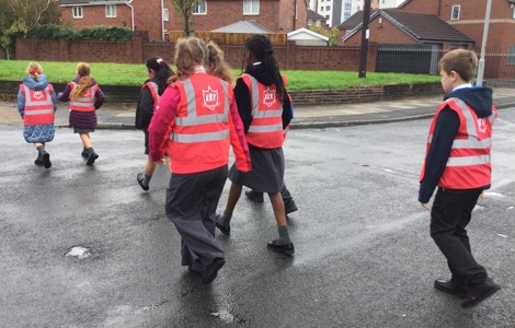 A photo of school children in pink high vis crossing a road