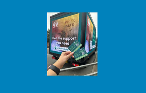 A person holds two green cards that say "We're here. Find the support you need. Search for seftonmind.org.uk" in front