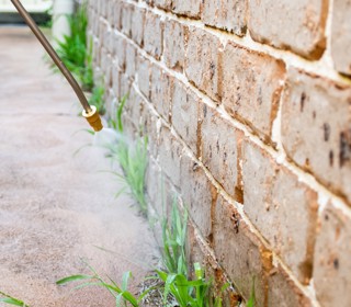 Nozzle spraying weeds alongside a brick wall